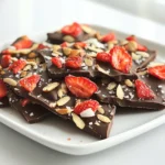 - 12 ounces dark chocolate chips - 1 cup dried strawberries (or freeze-dried) - ½ cup slivered almonds - ¼ cup coconut flakes (unsweetened) - Sea salt for sprinkling - 2 tablespoons coconut oil - Makes 12 pieces Each ingredient plays a key role in the taste and look of the bark. The dark chocolate chips offer a rich base. Dried or freeze-dried strawberries add a sweet and tangy flavor. Slivered almonds give a nice crunch. Coconut flakes bring a hint of tropical flavor. A sprinkle of sea salt adds depth. Optionally, coconut oil can make the chocolate smooth and glossy. This recipe yields 12 pieces of delicious bark, perfect for sharing or enjoying yourself! Start by lining your baking sheet with parchment paper. This step makes it easy to lift the bark off later. You want to make sure the paper covers the whole sheet so nothing sticks. Take a microwave-safe bowl and add 12 ounces of dark chocolate chips. If you like, add 2 tablespoons of coconut oil for a smoother finish. Heat the bowl in your microwave for 30 seconds. After that, take it out and stir. Repeat this until the chocolate is totally melted and smooth. This usually takes about 1 to 2 minutes total. Be careful not to overheat it. Now, pour the melted chocolate onto your lined baking sheet. Use a spatula to spread it evenly to about a ¼-inch thickness. Next, sprinkle 1 cup of dried strawberries, ½ cup of slivered almonds, and ¼ cup of coconut flakes on top. Press them down gently into the chocolate so they stick well. To finish, sprinkle a pinch of sea salt on top for extra flavor. Let your chocolate bark cool at room temperature for about 30 minutes. After that, place the baking sheet in the refrigerator. Chill it for about 1 hour, or until the chocolate is firm and set. Once it’s ready, break the bark into pieces that suit your taste. Enjoy your tasty treat! Melting chocolate can be tricky. You want to avoid seizing or burning it. Here are some tips to help: - Use a microwave-safe bowl. - Heat in 30-second bursts. - Stir each time to check the texture. - If chocolate gets too thick, add a little coconut oil. - Be patient; slow melting keeps it smooth. You can make this bark your own. Here are some fun ideas: - Try different toppings like nuts or seeds. - Add dried fruits such as apricots or cherries. - Use white or milk chocolate instead of dark. - Mix in spices, like cinnamon, for a kick. - Get creative! Your bark can reflect your taste. Make your bark look festive when serving. Here are some tips: - Use a decorative platter for a nice touch. - Arrange it with fresh strawberries for color. - Cut the bark into fun shapes or sizes. - Dust with extra coconut flakes for flair. - Enjoy sharing this treat at parties or gatherings! {{image_2}} You can switch up the chocolate for your bark. Try using white or milk chocolate instead of dark chocolate. Each type gives a different taste. White chocolate adds a sweet and creamy flavor. Milk chocolate is rich and smooth. These options can change the whole vibe of the treat. Feel free to mix and match, based on your mood or what you have on hand. You can get creative with your toppings too. Instead of just strawberries, try nuts like walnuts or pecans. Dried fruits like cranberries or apricots can add a chewy bite. You could even sprinkle some spices like cinnamon for a warm twist. The choices are endless, so have fun with it! If you need to follow special diets, you can easily adapt this recipe. For a vegan version, swap dark chocolate chips for dairy-free chocolate. Use a plant-based topping instead of slivered almonds. To make it gluten-free, just check that your toppings are safe. These simple changes let everyone enjoy this tasty treat! Store your chocolate covered strawberry bark in an airtight container. This keeps it fresh and tasty. You can use a glass jar or a plastic container with a tight lid. Make sure to layer the bark with parchment paper. This prevents sticking. The bark stays fresh for up to two weeks. If you keep it in the fridge, it may last longer. Always check for any signs of spoilage before eating. If it smells off or has a weird texture, toss it out. Yes, you can freeze chocolate bark! Wrap it well in plastic wrap and then put it in a freezer bag. This helps prevent freezer burn. When you want to eat it, let it thaw at room temperature. Enjoy it cold or at room temp! Making chocolate covered strawberry bark is easy and fun. First, gather your ingredients. You need dark chocolate chips, dried strawberries, slivered almonds, coconut flakes, and sea salt. You can add coconut oil for a smooth texture if you want. Start by lining a baking sheet with parchment paper. Then, melt the dark chocolate in a microwave-safe bowl. Heat it in 30-second bursts, stirring in between. Once smooth, pour the chocolate onto the baking sheet. Spread it evenly to about ¼ inch thick. Next, sprinkle dried strawberries, slivered almonds, and coconut flakes over the melted chocolate. Lightly press the toppings in. Finish by adding a pinch of sea salt for flavor. Let it cool at room temperature for 30 minutes. Then, chill it in the fridge for about an hour until set. Break the bark into pieces, and enjoy! You can use fresh strawberries, but there are pros and cons. Fresh strawberries add great flavor and color, but they have more moisture. This moisture can make the chocolate soggy and affect the bark's texture. Dried strawberries have a chewy texture and concentrate their sweetness. They also stay crunchy when mixed with chocolate. If you choose fresh strawberries, slice them thin and dry them on paper towels to reduce moisture. If your chocolate isn't setting, it could be due to moisture. Even a small amount can cause issues. Make sure your bowl and baking sheet are completely dry. Another reason could be overheating the chocolate. If you burn the chocolate, it can seize and become thick. Always melt it slowly in short intervals. If your chocolate is not setting, try placing it in the fridge for longer. Yes, you can make chocolate covered strawberry bark ahead of time. It stores well in an airtight container. Just keep it in a cool, dry place. The bark stays fresh for up to two weeks. If you want to keep it longer, you can freeze it. Wrap the pieces in plastic wrap, then place them in a freezer bag. When ready to eat, thaw the pieces at room temperature. You’ve learned how to make tasty chocolate bark. We covered the main ingredients and the fun toppings you can try. Followed my simple steps, you can melt your chocolate, mix in your favorites, and let it set. Remember, you can customize it to fit your taste. Whether you want it sweet or crunchy, you have choices. Store it well, and enjoy it for weeks. Cooking can be fun and creative, so get started and make your own chocolate bark today!